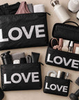 Set of four black travel pouches with silver LOVE text with various workout and beauty items on beige background