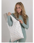 Woman in green athletic apparel holding a yoga pose print tote bag with yoga mat inside.
