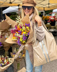 Woman holding flowers and carryall tote in shimmer beige with silver stripes at farmers market