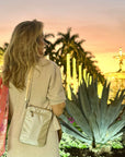 Woman with a golden handbag standing in a garden with palm trees and a fountain at sunset.
