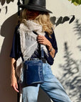 Woman wearing a navy blue crossbody purse leaning against a cement wall with shadows of plants reflected on the wall.
