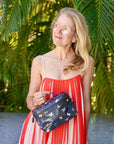 Woman in a red dress holding a butterfly-patterned pouch with greenery in the background
