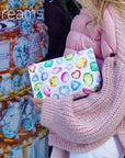 Person holding a colorful pouch with gemstone patterns in front of a decorative wall.