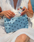 Person grabbing sunscreen from cosmetic zipper pouch light blue shimmer myriad stars