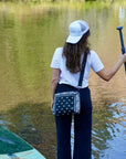 Woman paddleboarding on water with crossbody purse in black bandana print