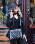 Women standing in black hat outdoors carrying crossbody purse in black bandana print