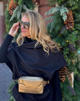 A woman wearing a black outfit with a gold crossbody fanny pack belt bag near holiday greenery