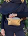 Person wearing a gold fanny pack belt bag with a black outfit against a festive background