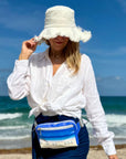 Woman on a beach wearing a white hat and white shirt with puffer crossbody fanny pack belt bag on harbor island beach print