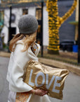 Woman holding a large zipper pouch with 'LOVE' printed
with festive lights in the background