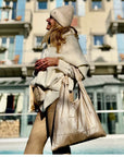 Women wearing a beige tote back with beige clothing next to hotel with blue shutters