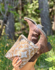 Medium Shimmer Bronze Bandana Print zipper pouch held beside brown cowboy boots in an outdoor setting.
