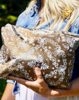 Woman in a denim shirt holding a Medium Shimmer Bronze Bandana Print zipper pouch outdoors.