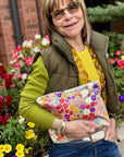 Woman in green sweater and vest near flowers holding medium zipper pouch in watercolor poppies pattern