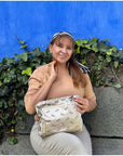Women carrying beige bandana print clutch sitting on a bench with greenery and a bright blue wall