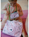 Little girl holding a pink pouch with paisley bandana heart patterns on a pink rug