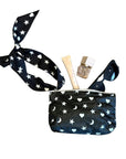 A black zippered pouch with a matching silk tie strap, decorated with a white star and moon pattern, shown with cosmetic items inside on a plain white background.