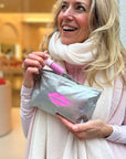 Woman holding a silver pouch with pink lip print in a store setting