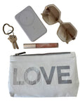 Small White pouch with LOVE printed on it with sunglasses, lip balm, charger and keys on white background