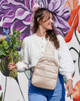 Girl holding flowers and puffer crossbody backpack in shimmer beige on floral wall background