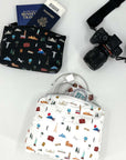 Two patterned pouches with travel-themed designs, a camera, and passport on a white surface.