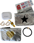 A curated flat-lay of silver metallic zip pouches with heart and star designs, shown alongside accessories including a white AirPods case with 'HI LOVE' printed on it, heart-shaped earings, a mint, credit card, a black braided hair tie with a heart charm, and a package of Tylenol and bandaid.