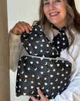 Woman wearing a white blouse holding two zipper pouches in shimmer black with heart moon star print on them.