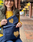 Woman holding two blue bags with gold hearts on a sidewalk
