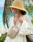 Women by beach wearing Puffer Crossbody Fanny Pack Belt Bag in Golden Shimmer Beige