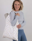 Woman holding a white tote bag with colorful yoga pose pattern against a plain background