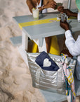 Silver puffer tote with a shimmer navy mini pouch sitting on a bench on the sand