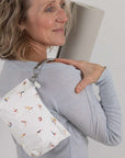 Woman holding a white pouch with colorful yoga poses on a plain background