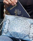 Close up of hand putting passport into blue travel pouch wristlet with bandana print against dark background
