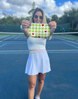 Woman holding a tennis ball and heart print wristlet bag on a tennis court