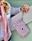 Person holding a pink bandana patterned pouch with a strap against a light green background