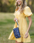 Woman in a yellow dress holding a blue bag with white stars outdoors.