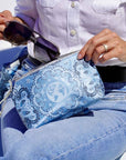 Close up of hand putting sunglasses into blue travel pouch wristlet with bandana print against light background