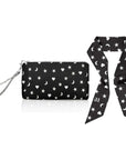A black wristlet pouch with a silver wrist strap, decorated with a white celestial pattern of stars, moons, and hearts, shown next to a matching black and white silk scarfette on a white background.