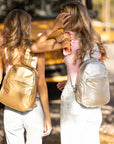 Two teens wearing gold and silver sling backpacks