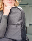 Woman resting her chin on her hand beside the black signature backpack near a plane door.