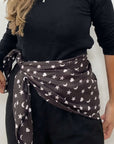 Model wearing the black Signature scarf with white hearts, moons and stars tied around her waist over a black outfit.