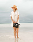 Woman holding a black 'LOVE' pouch on a beach