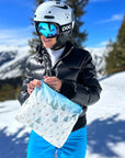 Women in wearing ski helmet and goggles holding the bluebird ski day medium zipper pouch