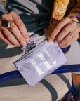 Person holding a small purple pouch with 'H.' on it, sitting outdoors.
