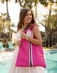 Smiling woman in front of a pool wearing hot pink carryall tote bag.