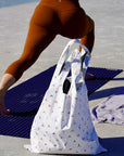 Person on a beach with a white tote bag featuring colorful yoga designs.
