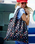 Woman in red hat and sunglasses stepping into plane holding black travel inspired pattern of landmarks from the seven continents.