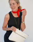 Woman holding a white handbag with a red scarf around her neck against a plain background