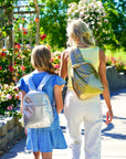 Mother and daughter walking holding hands wearing coordinated silver and gold backpacks