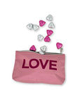 Cosmetic zipper pouch in pink with pink love and heart candies laying around it on white background